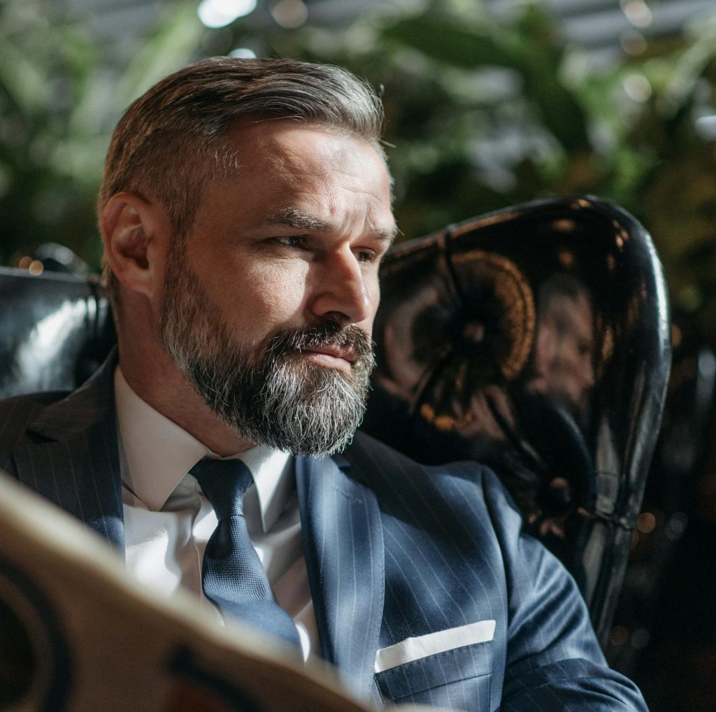 Professional businessman with beard reads a newspaper indoors in a formal setting.